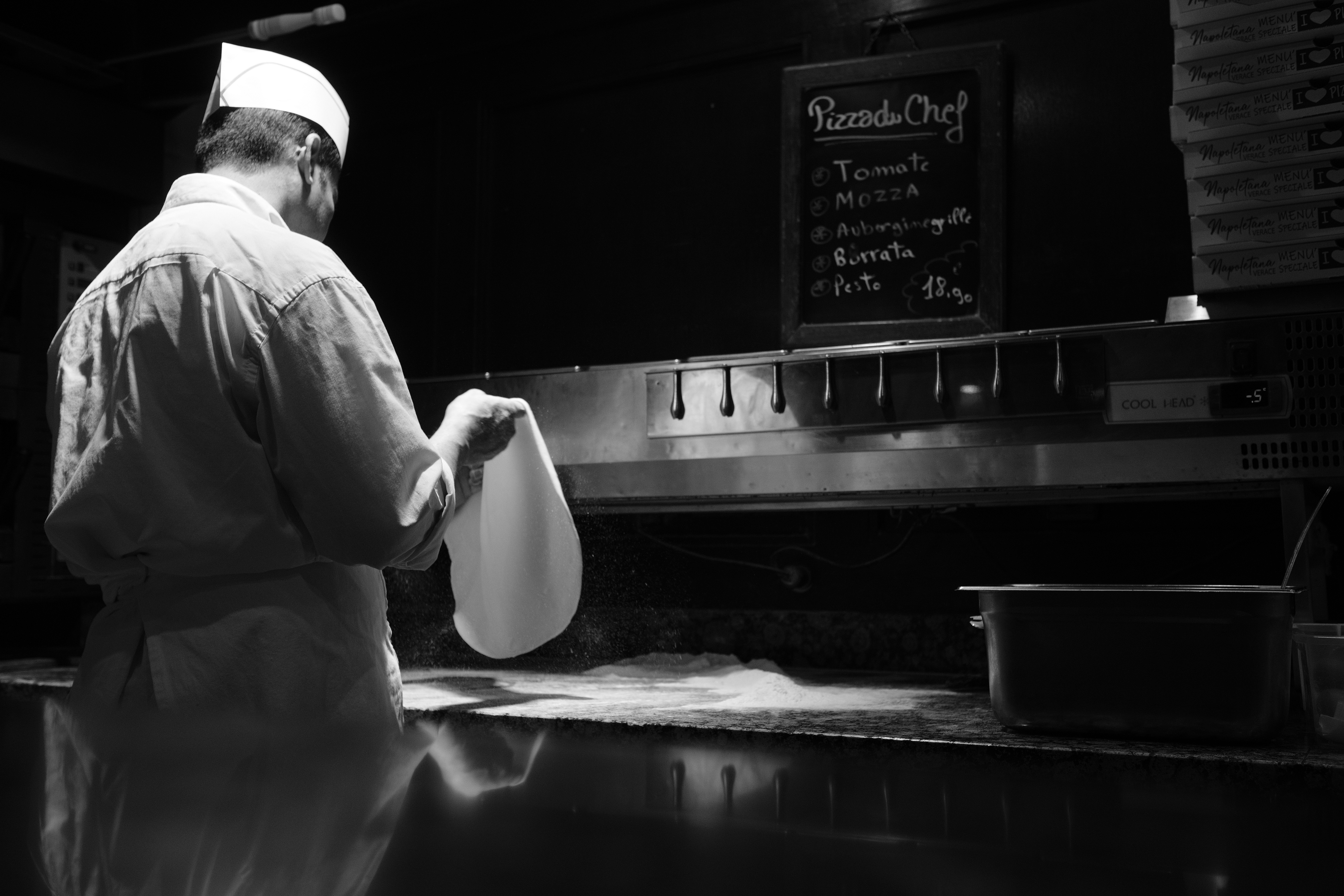 A pizzaiolo stretching dough in a Paris kitchen, photographed in black and white